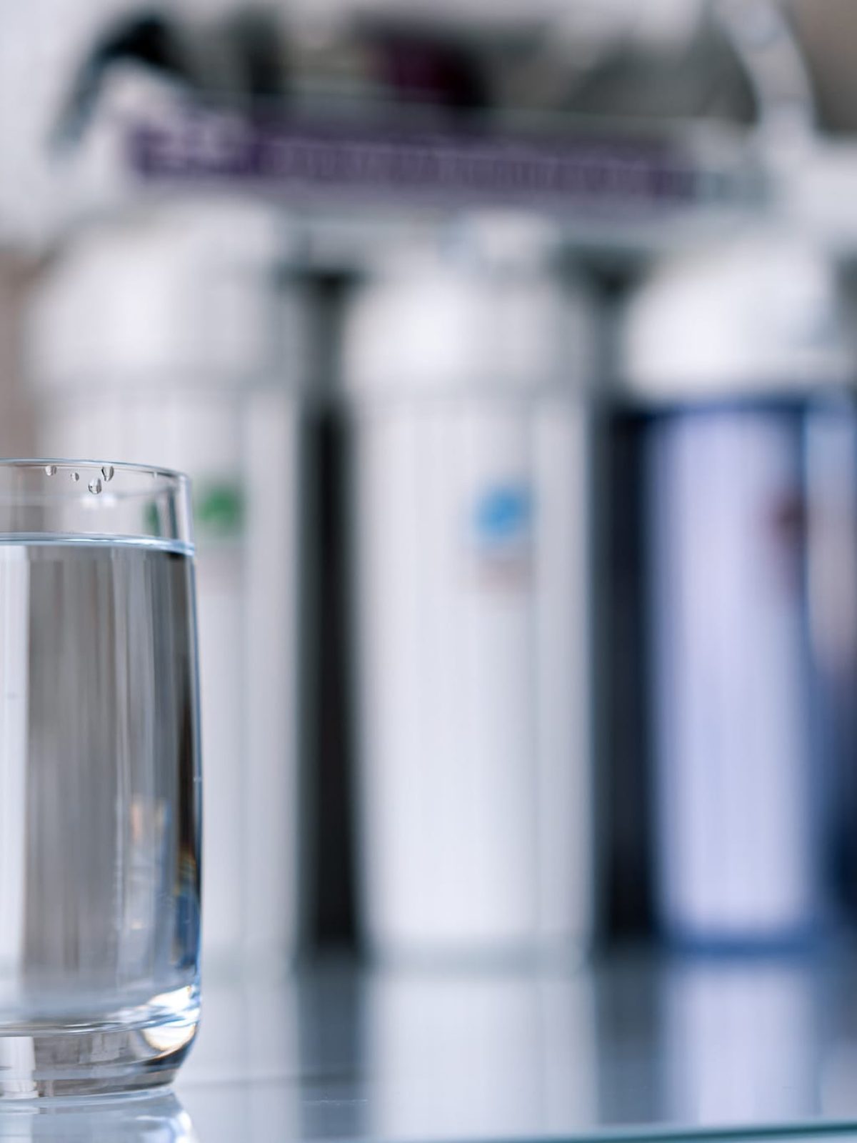Pure water in glass and water filters on the blurred background. Household filtration system. Pure water in glass and water filters on the blurred background. Household filtration system.